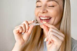 Happy woman putting on her retainer to maintain her new perfect smile after braces