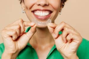 A woman smiling and holding an Invisalign aligner