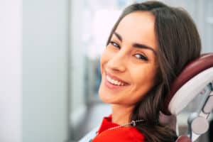 A woman sitting in a dentist's chair and smiling after orthognathic surgery in Denver