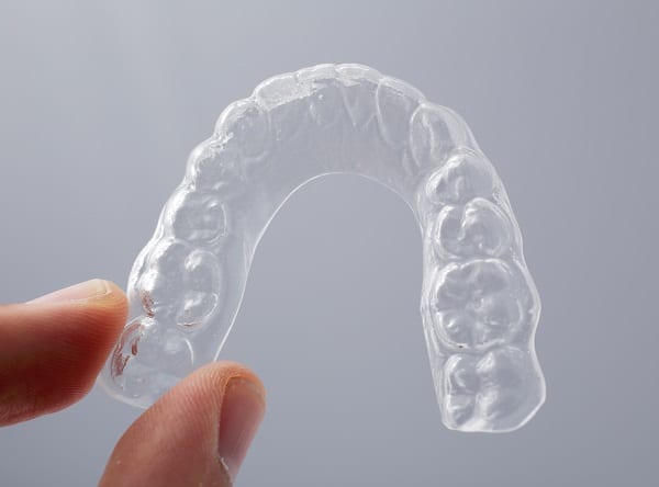 Hand holding a translucent upper essix retainer 1766076324 Retainer Essix 1 Retainers in Denver, CO