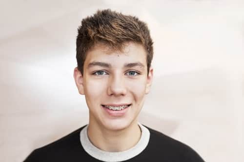 A boy smiles at the abstract background and his braces are clearly visible on his teeth 1766076368 braces male student 1 Orthodontics in Denver CO