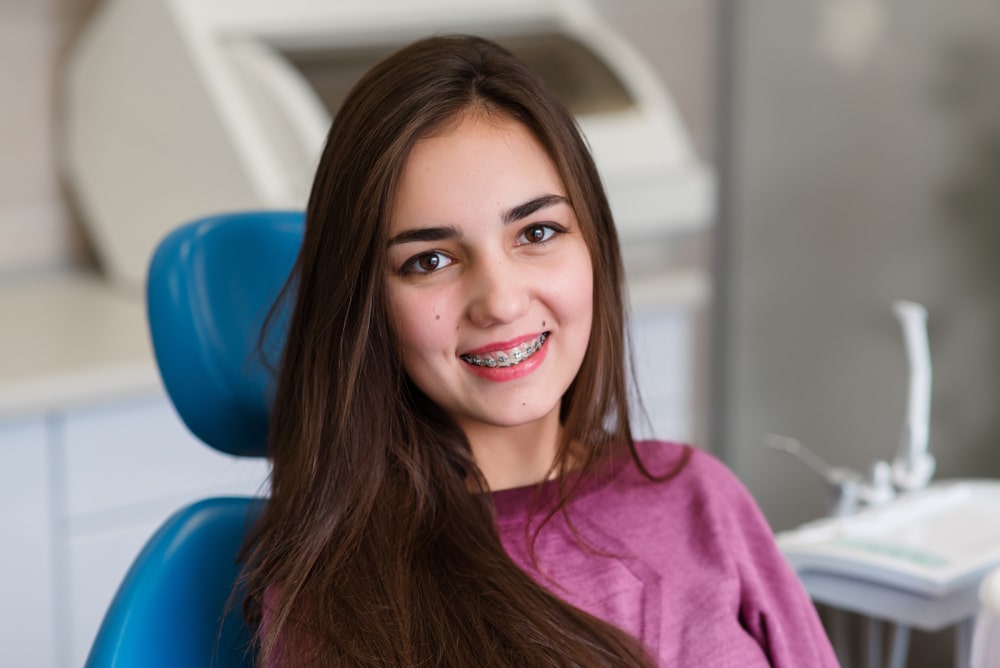 A girl with braces smiling in an orthodontist's chair