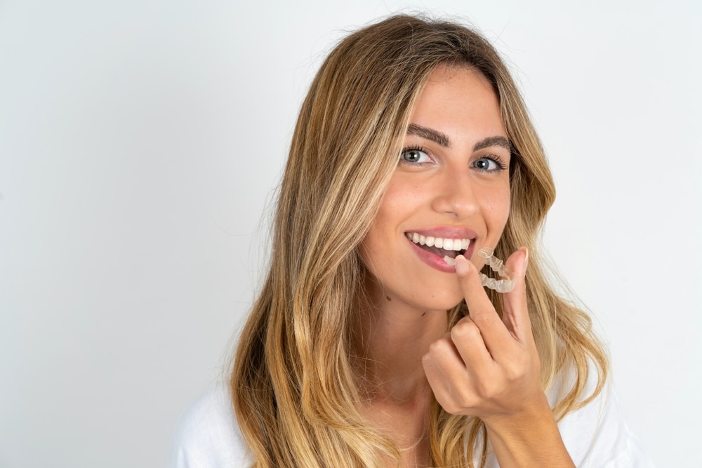 A woman smiling and holding an Invisalign® aligner