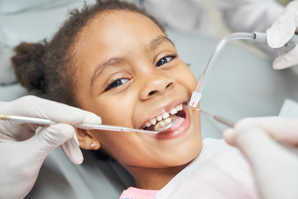 Child smiling during a dental-style exam, representing an early orthodontic visit to check tooth and jaw development.
